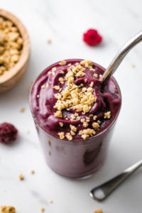 side angle view of acai smoothie with granola and items surrounding.