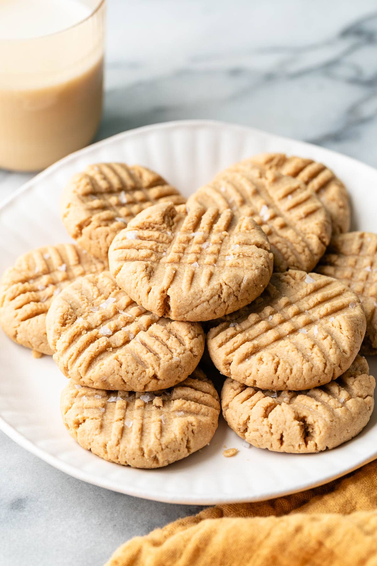 side angle view of gluten free peanut butter cookies on a white plate with items surrounding.