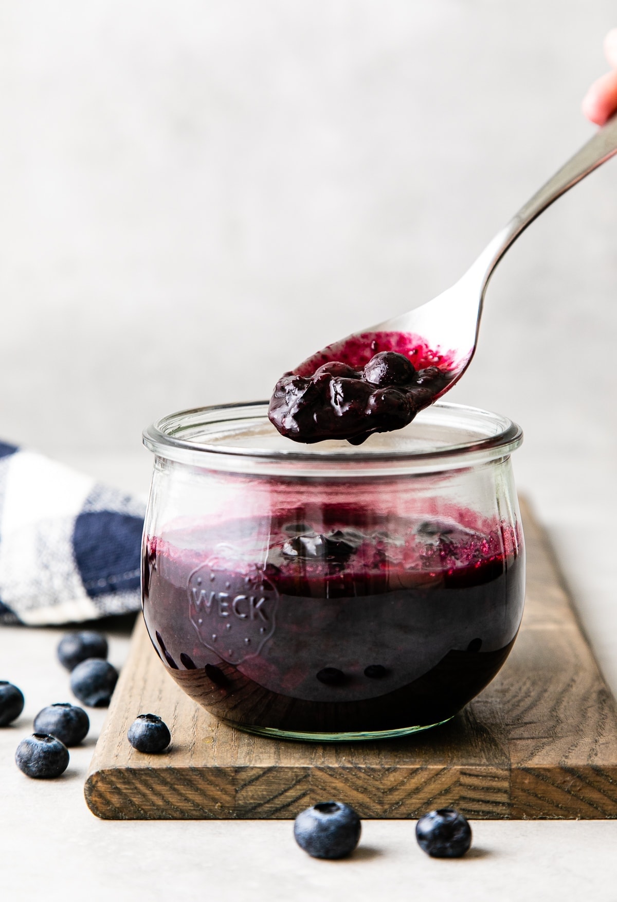 head on view of glass jar of blueberry compote with a spoon with scoop over top.