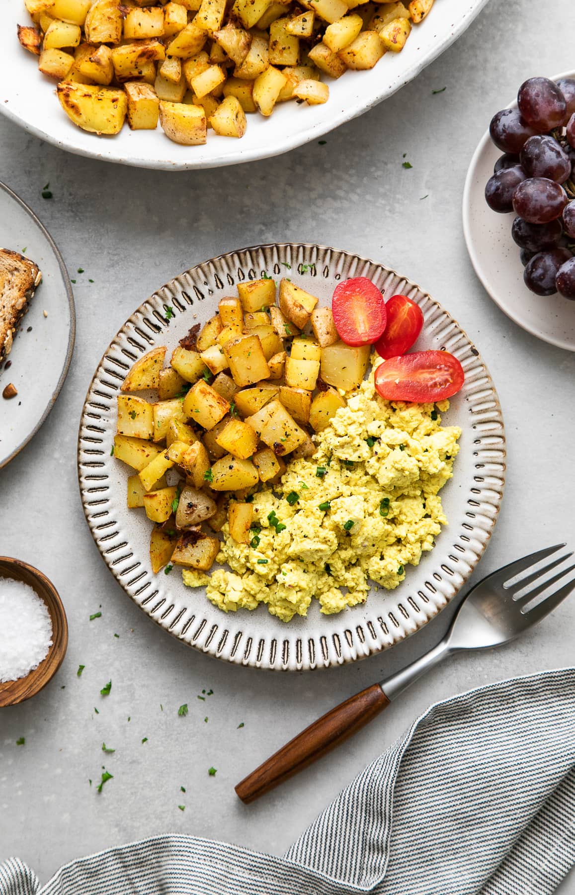 top down view of the best ever breakfast potatoes with tofu scramble on a small plate and items surrounding.