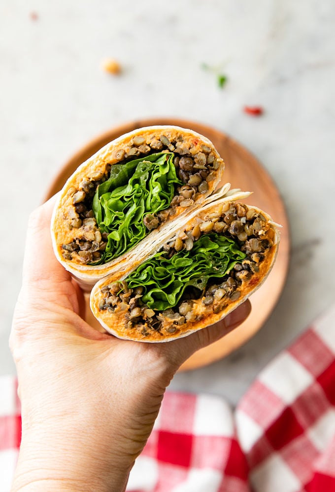 top down view of hand holding two halves of lentil wrap with sun-dried tomatoes hummus.