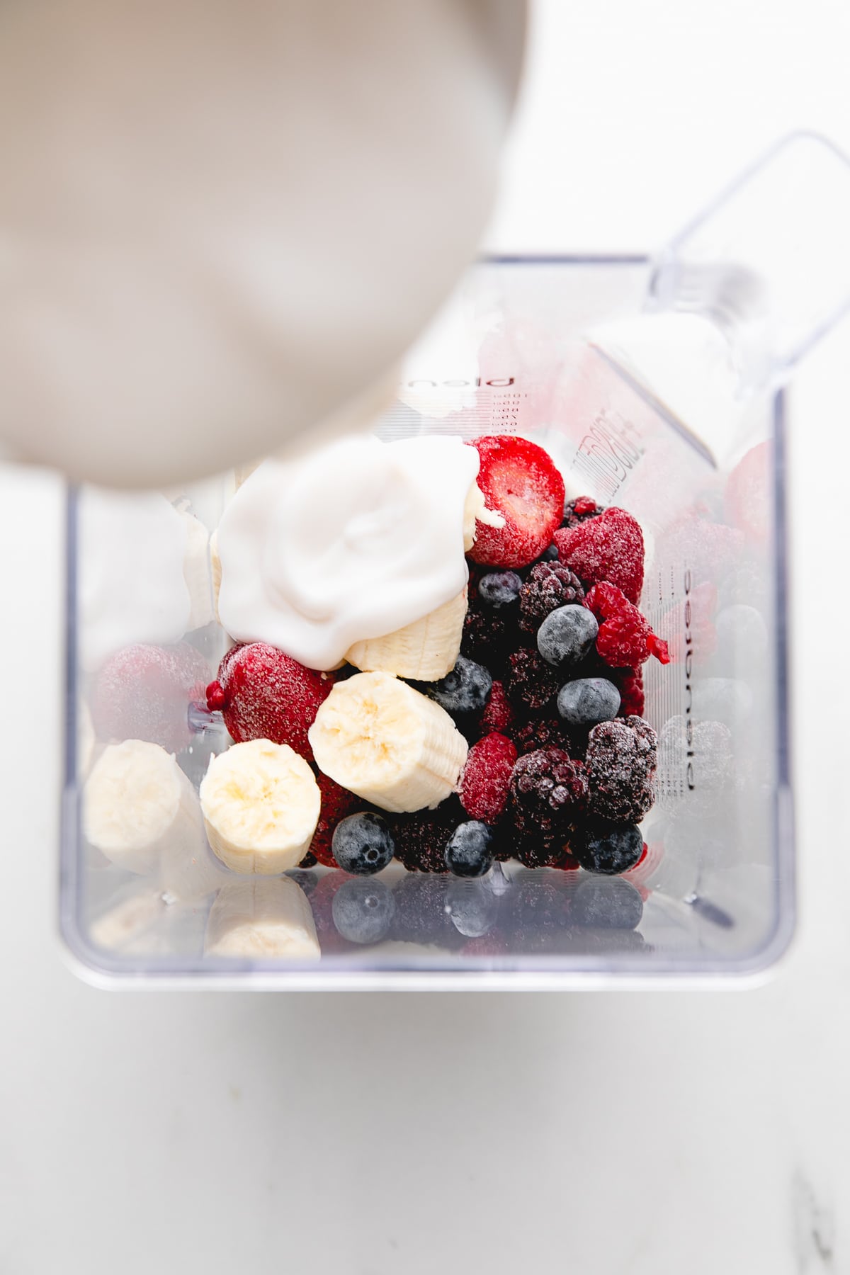 top down view of yogurt smoothie ingredients added to blender cup.