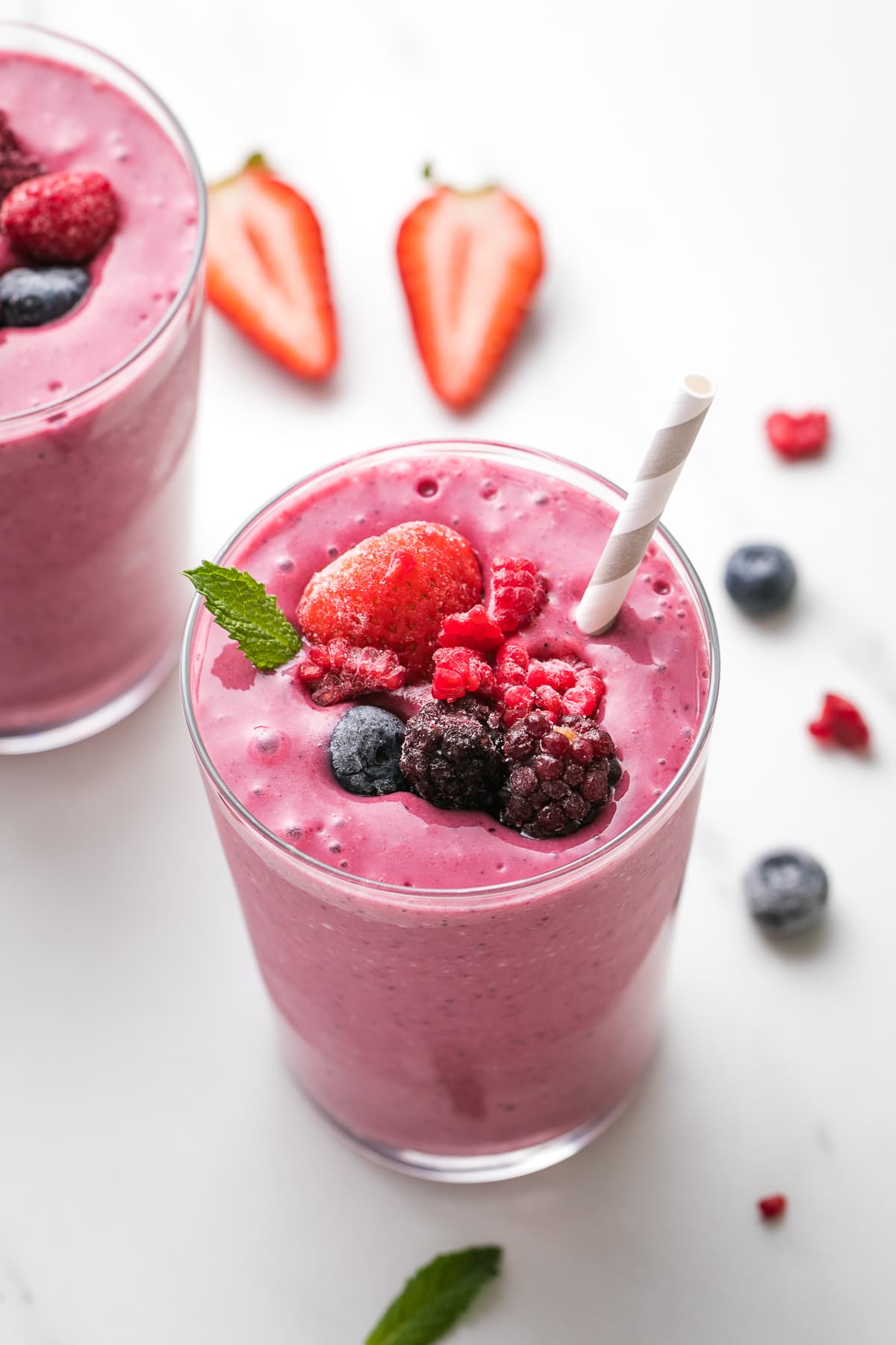 side angle view of healthy mixed berry yogurt smoothie in a glass with straw and items surrounding.