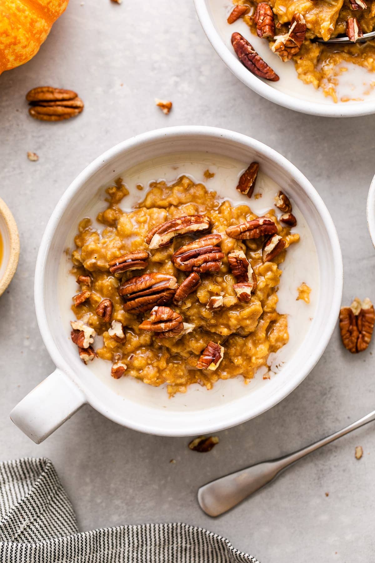 top down view of healthy pumpkin oatmeal in a whole bowl with handle and items surrounding.