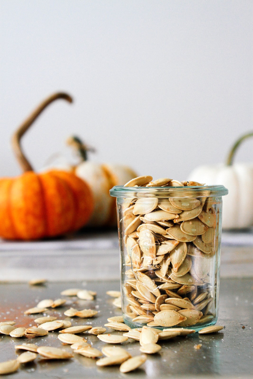 head on view of roasted pumpkin seeds in a glass jar with items surrounding.