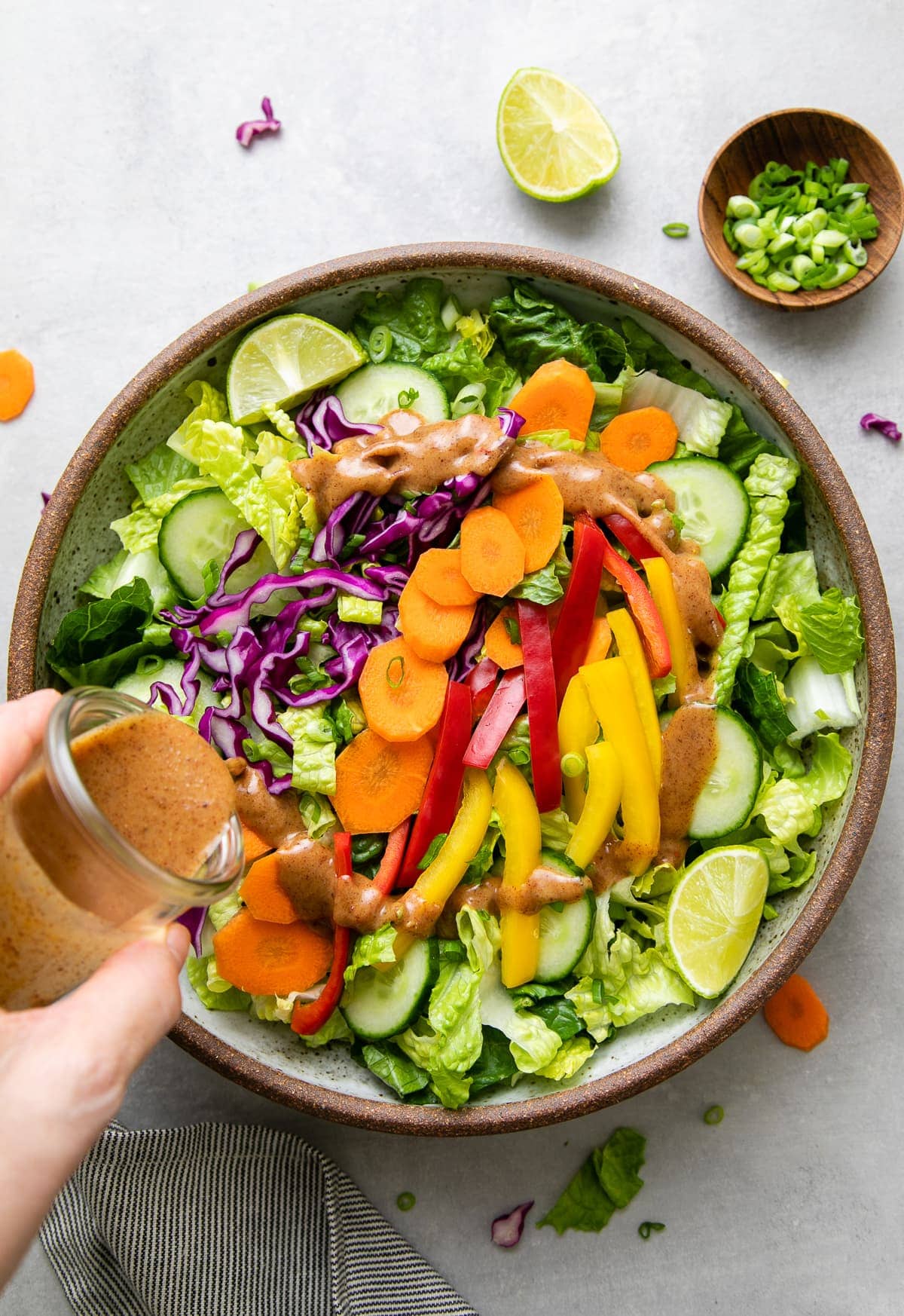 top down view of creamy almond dressing being poured over romaine salad.