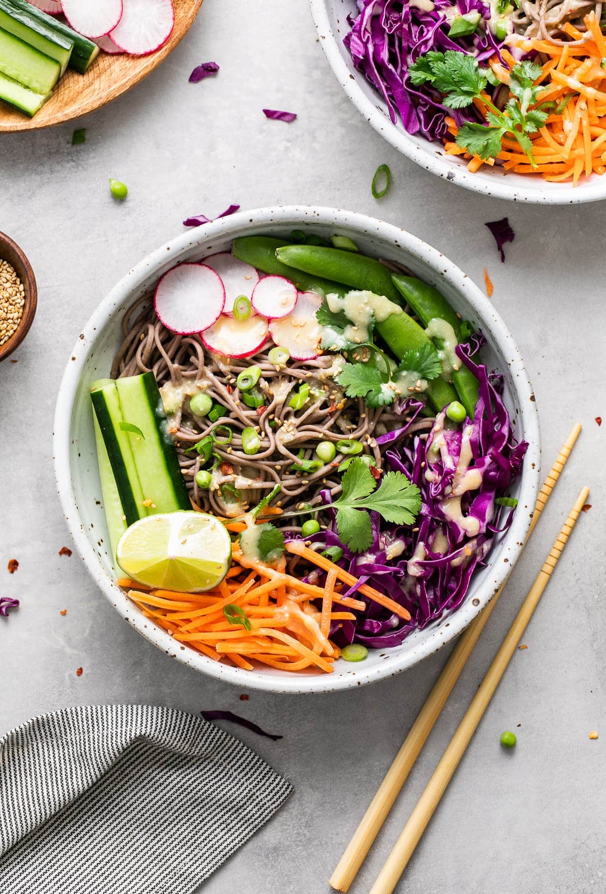 top down view of cold soba noodle bowl with with veggies and miso dressing and items surrounding.