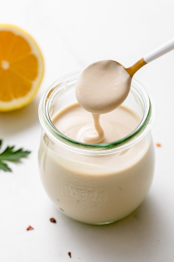 side angle view of spoonful of tahini sauce spilling into a glass jar.