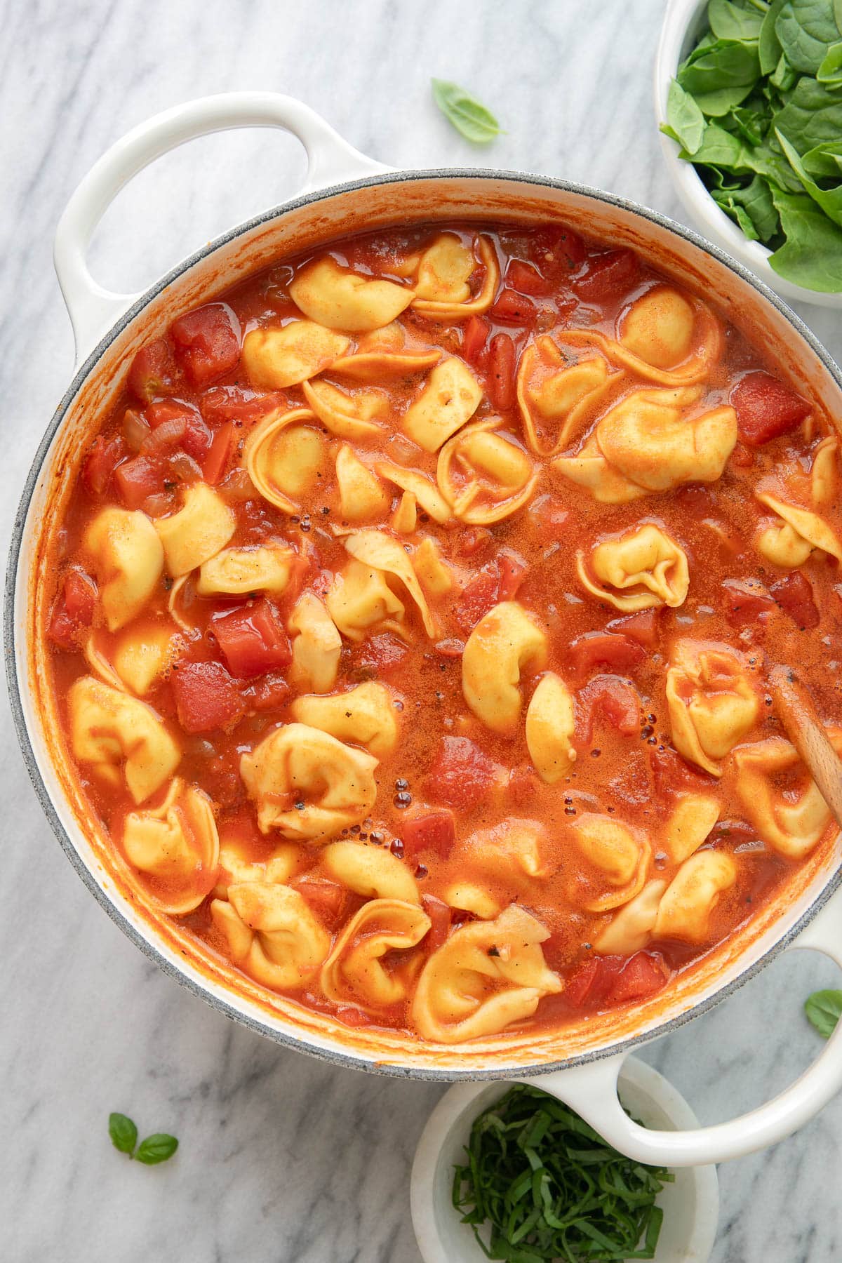 top down view of simmering tomato tortellini soup in a white pot.