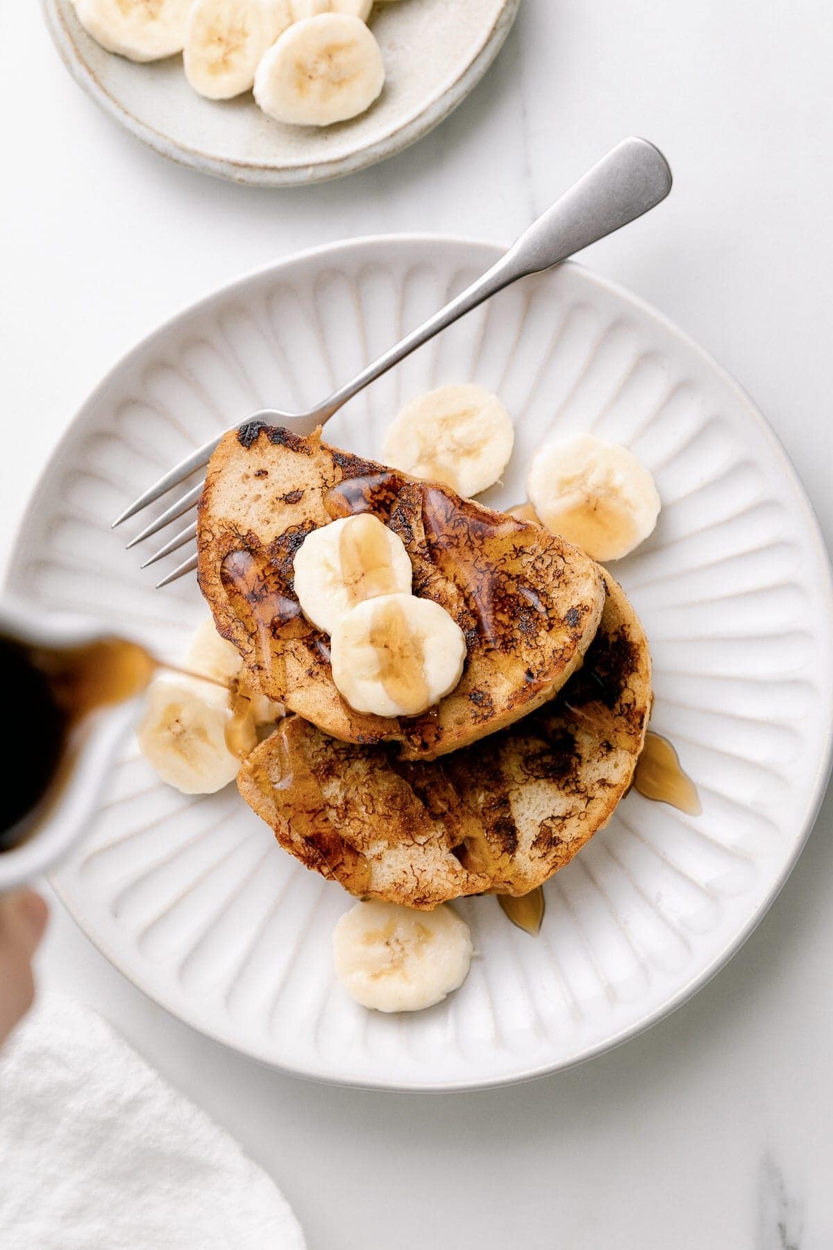 top down view of plated vegan banana french toast with syrup being poured over top.