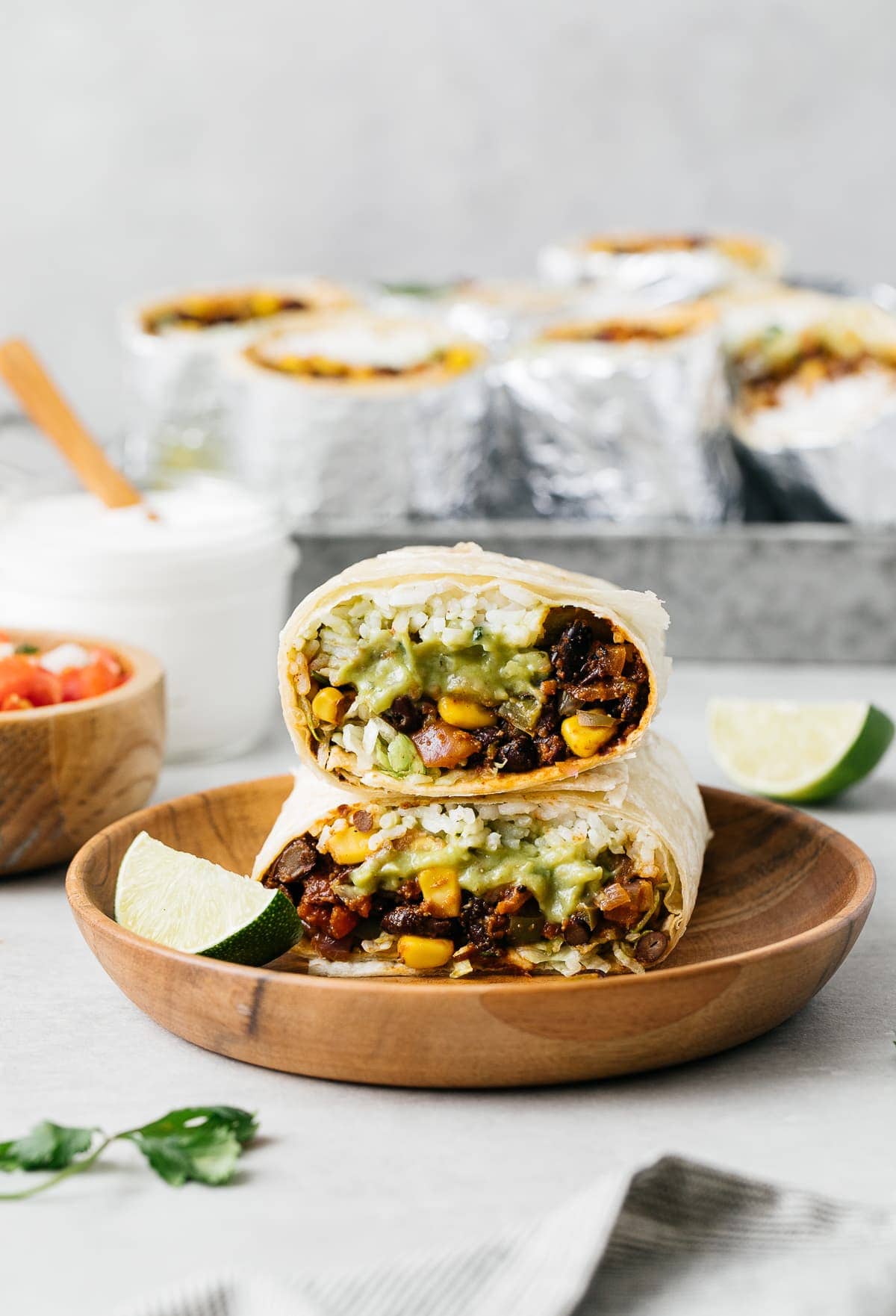 head on view of 2 halves of vegan burrito stacked on each other with items surrounding.