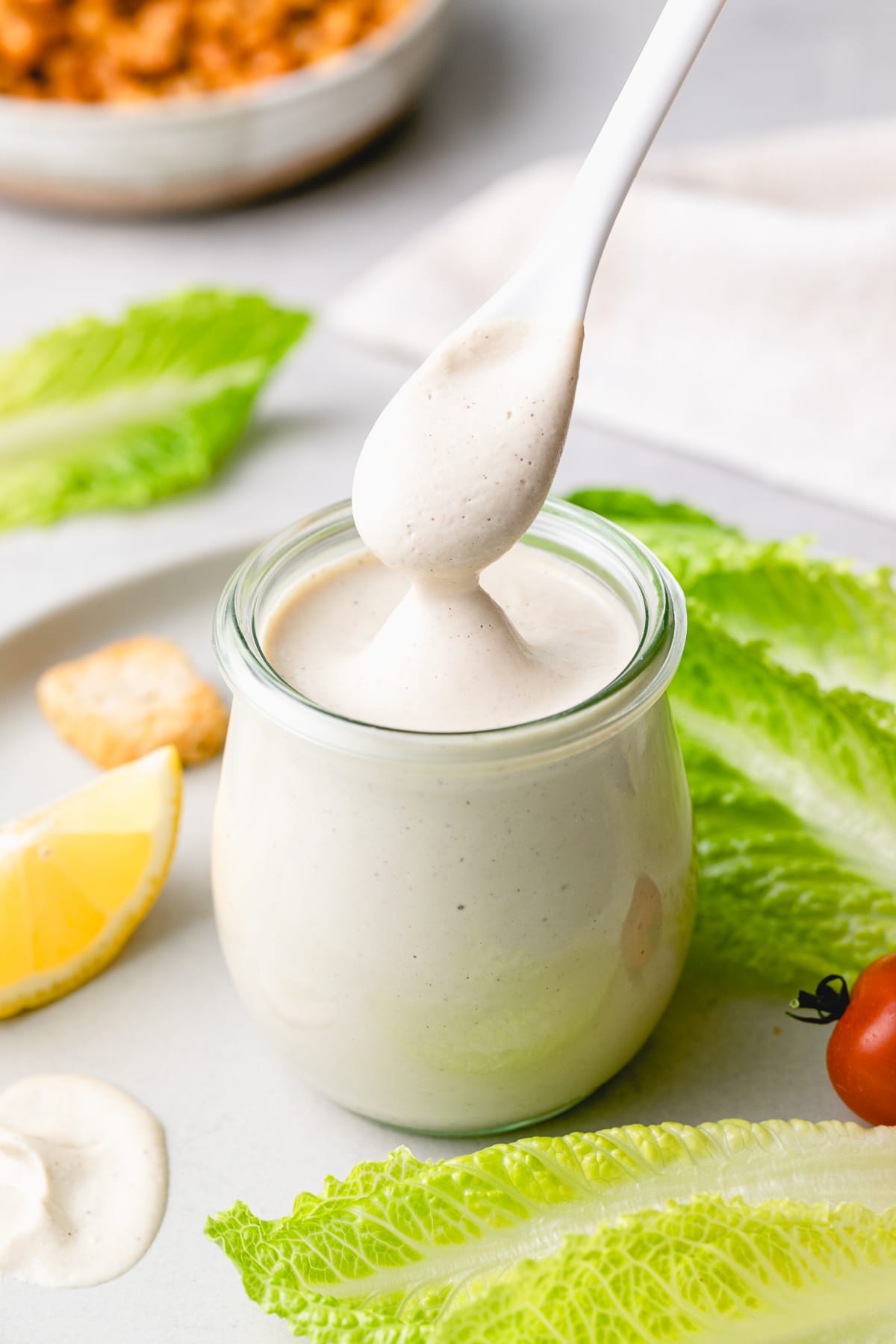 head on view of glass jar full of vegan caesar dressing with spoon.