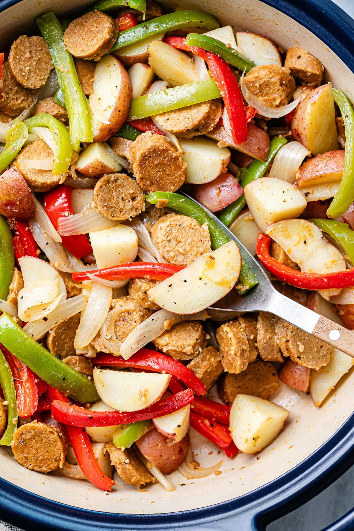 top down view of freshly made vegan kielbasa sausage with potatoes and peppers in a pot with wooden spoon.