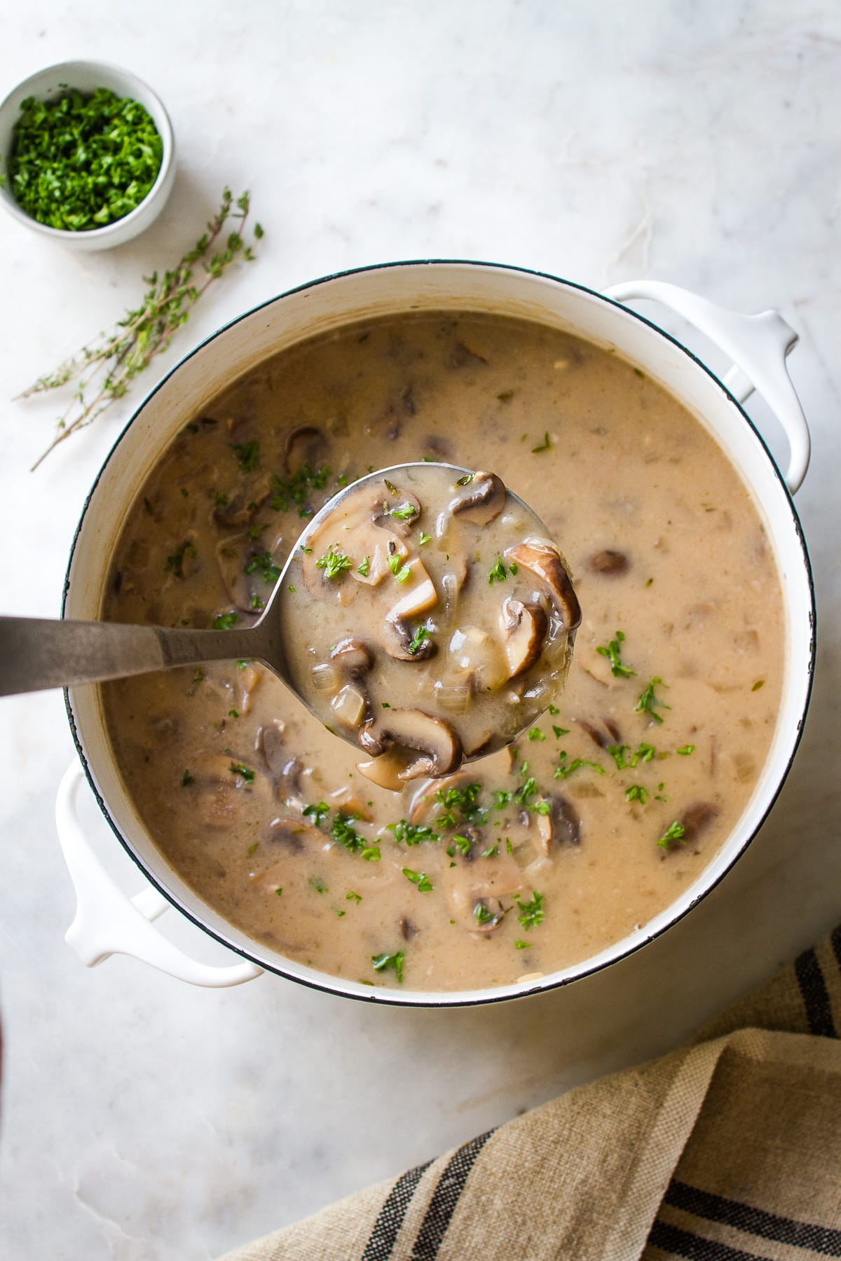 top down view of a white pot of vegan mushroom soup with a ladle full of soup.