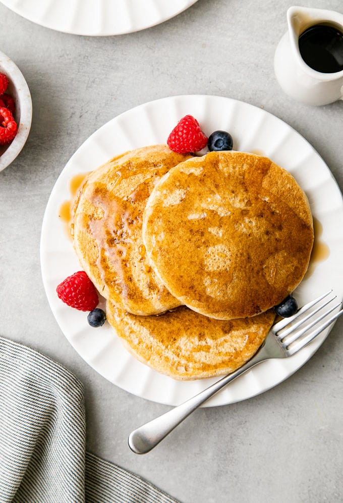 top down view of serving of vegan pancakes on a small plate with items surrounding.