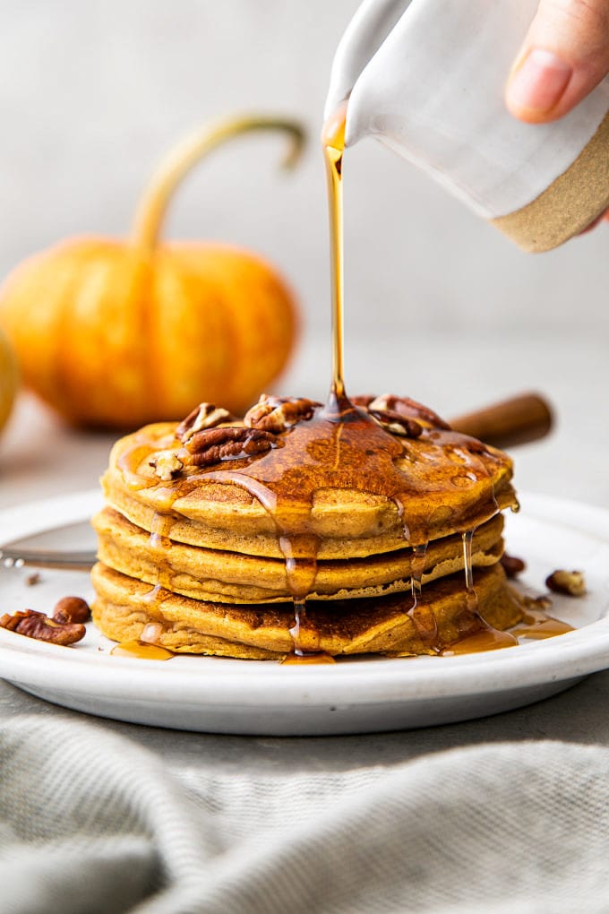 head on view of maple syrup being poured overtop vegan pumpkin pancakes.