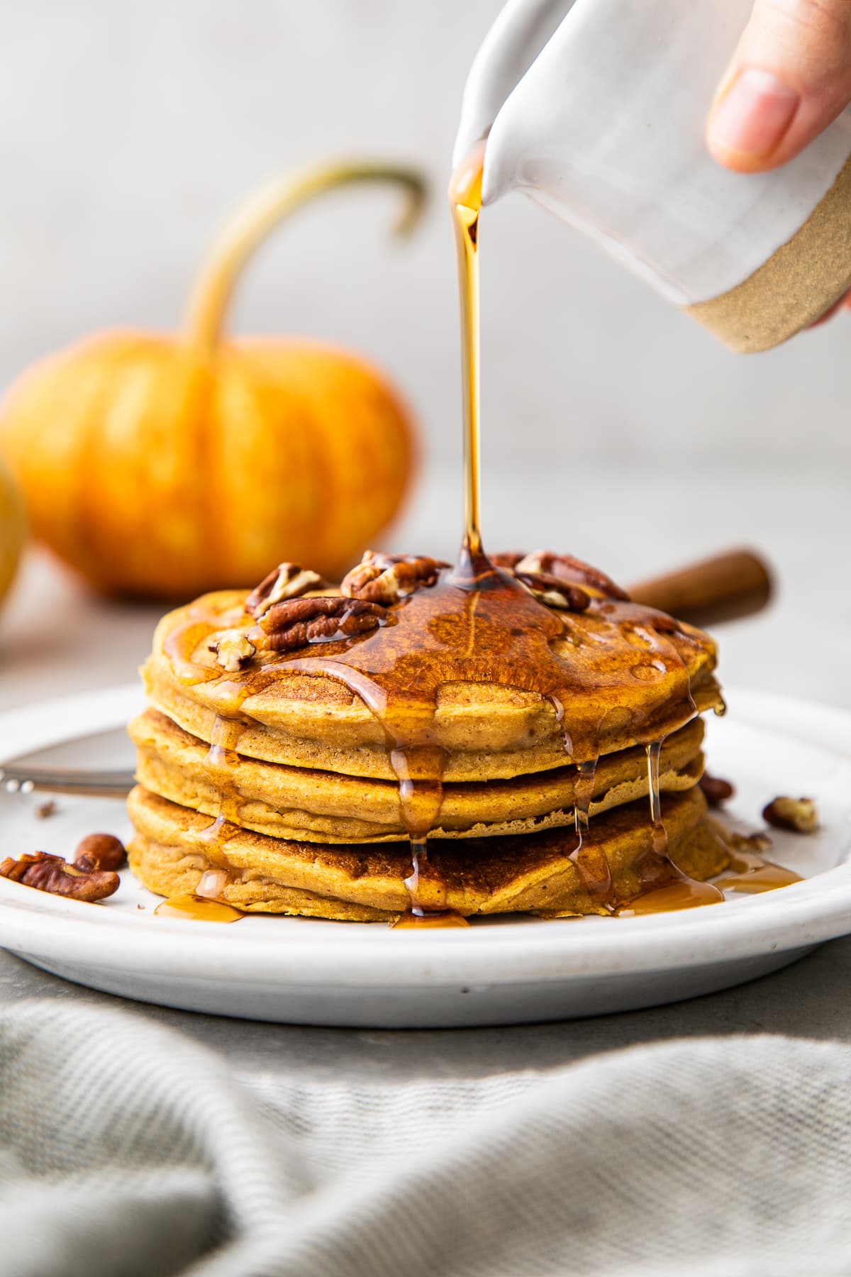 head on view of maple syrup being poured overtop vegan pumpkin pancakes.