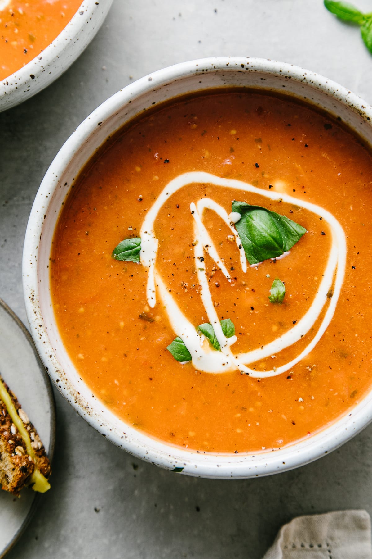 top down view of bowl with serving of tomato basil soup and items surrounding.