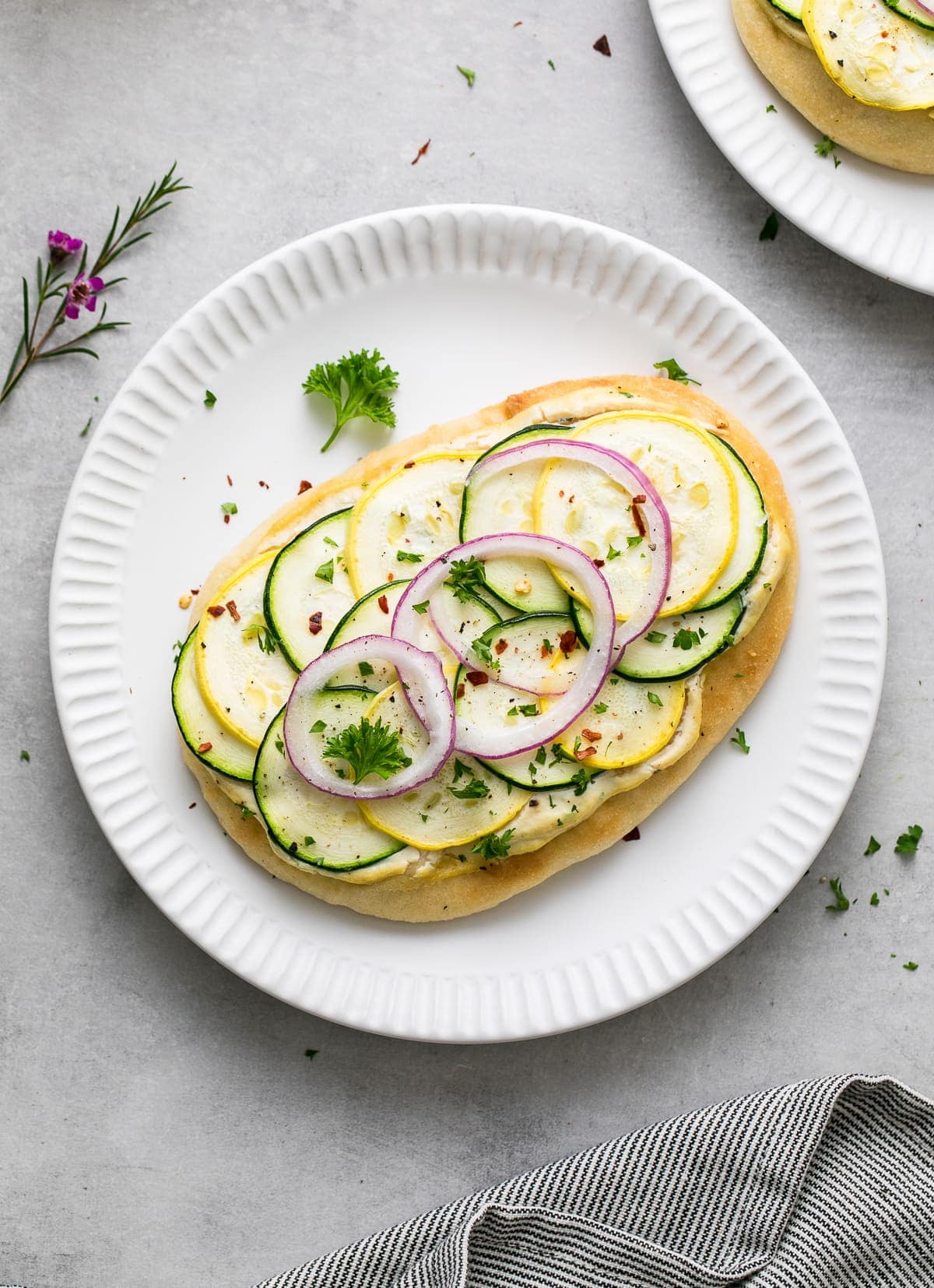 top down view of vegan flatbread white pizza with zucchini on a small white plate.