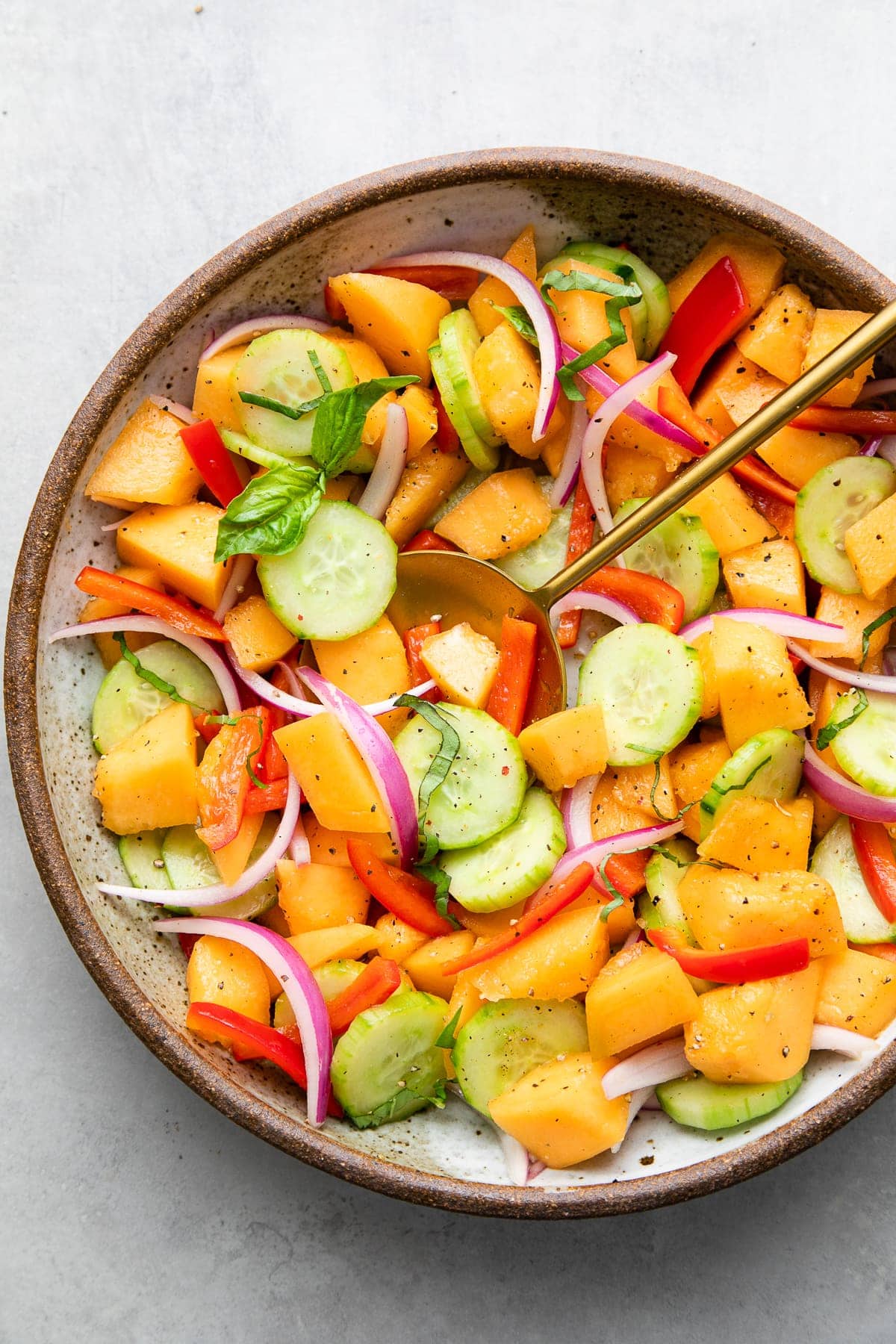 top down view of cantaloupe cucumber salad in a serving bowl with serving spoon and topped with basil.