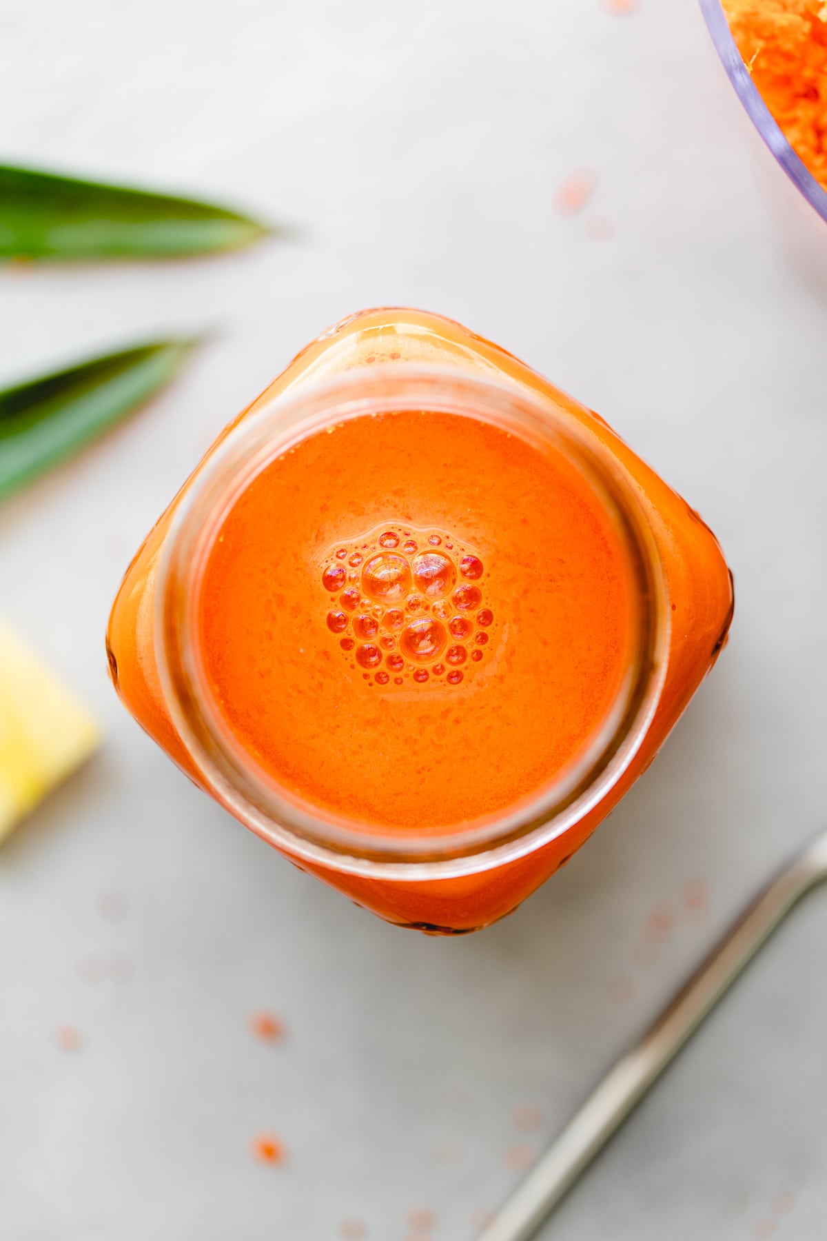 top down view of carrot pineapple juice with ginger in a glass with items surrounding