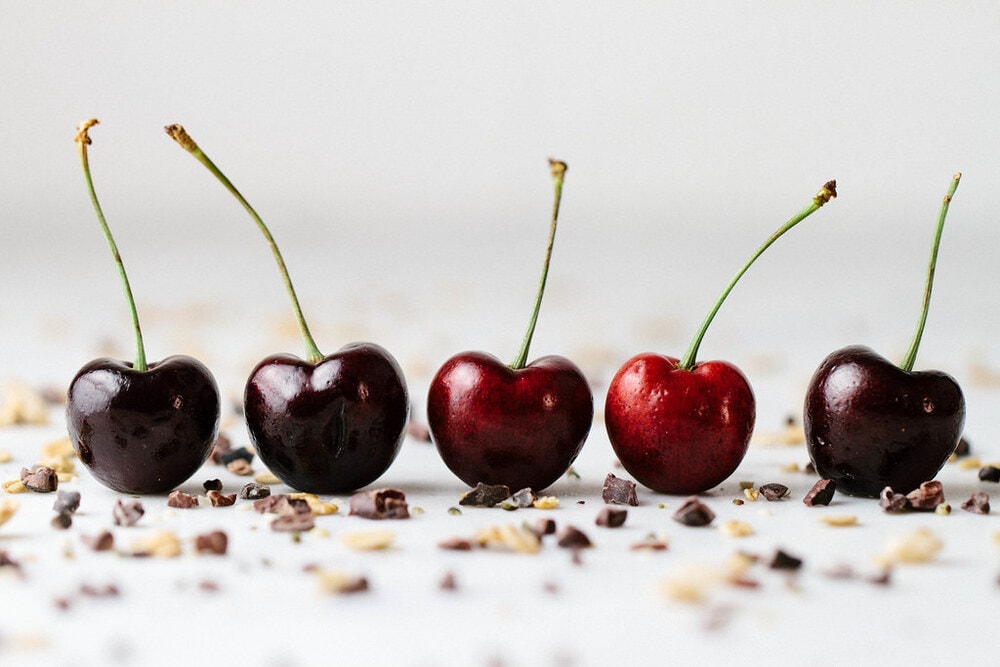 head on picture of 5 cherries lined up in a row with cacao nibs sprinkled all around. 