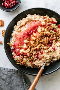 top down view of cinnamon oatmeal with applesauce, pecans, apples, pomegranetes in a black bowl