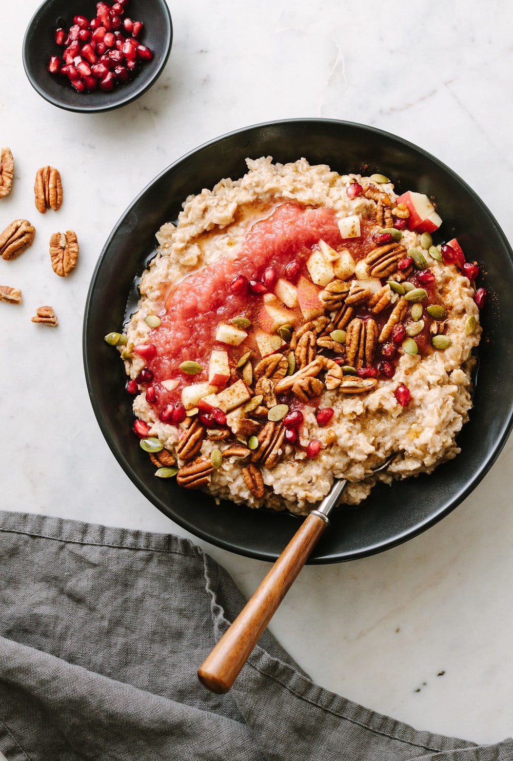 cinnamon oatmeal with applesauce, pecans, apples, pomegranetes in a black bowl