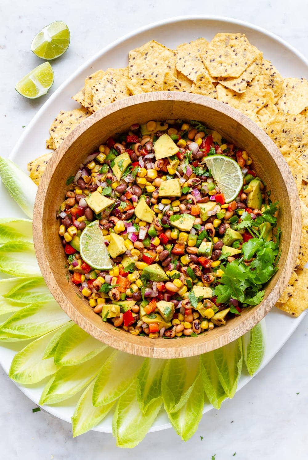 top down view of a platter with bowl full of cowboy caviar surrounded by endive and tortilla chips for scooping.