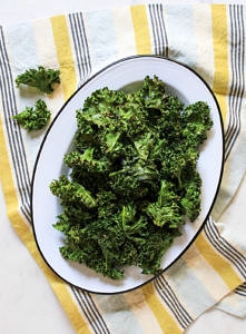 crispy baked kale chips on an oval white plate with black rim