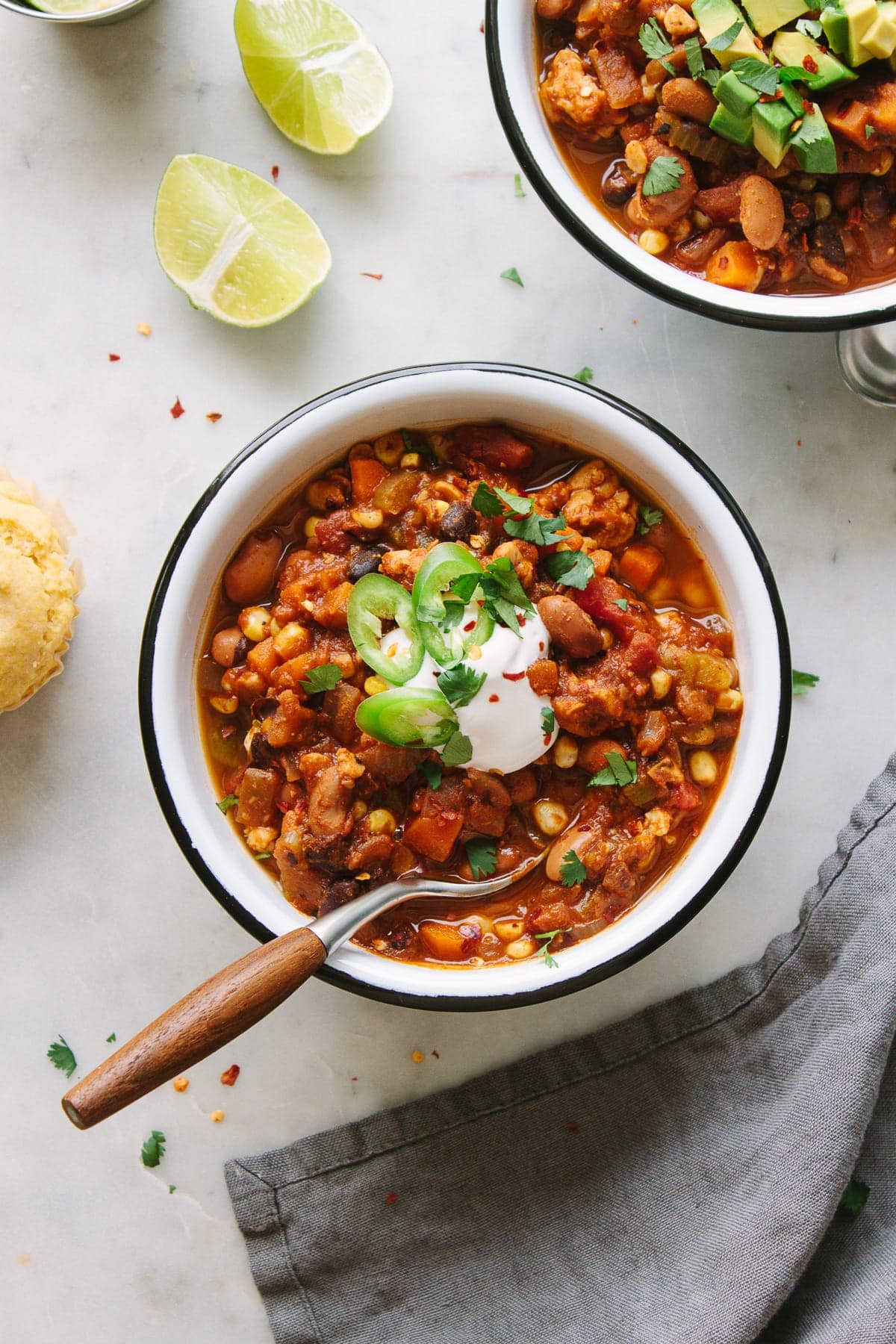 top down view of a serving of easy vegetable chili in a white bowl with black rim and wooden spoon.