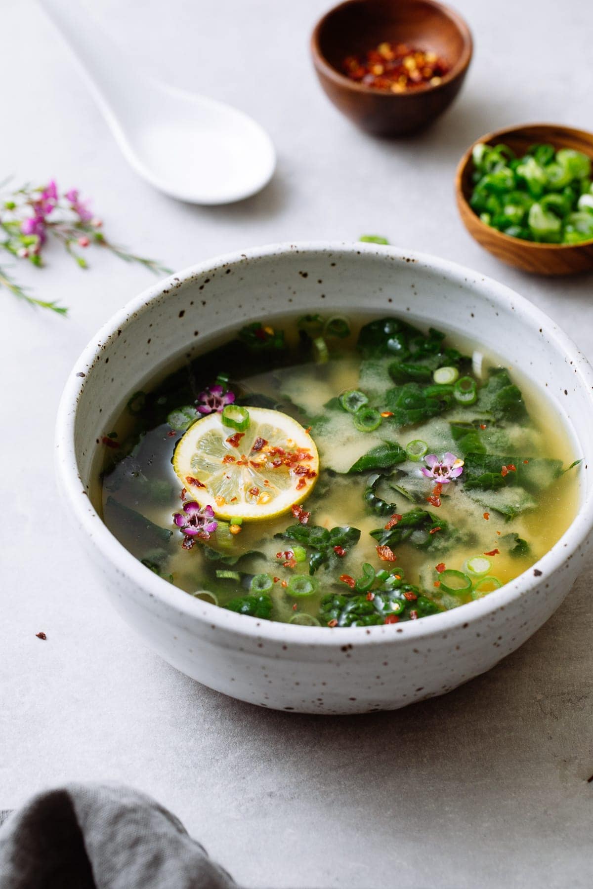 side angle view of bowl with serving of garlic miso soup with kale and items surrounding.