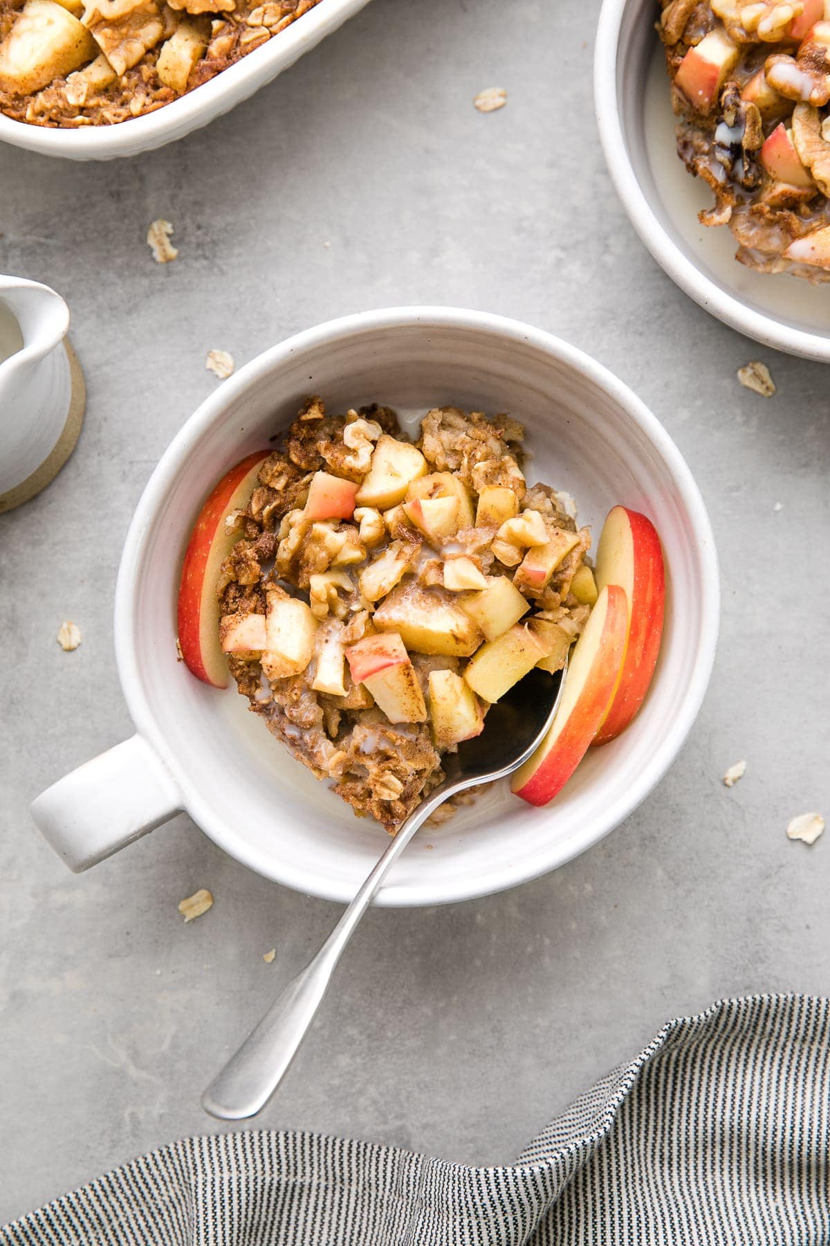 top down down of healthy apple baked oatmeal in a bowl with spoon and items surrounding.