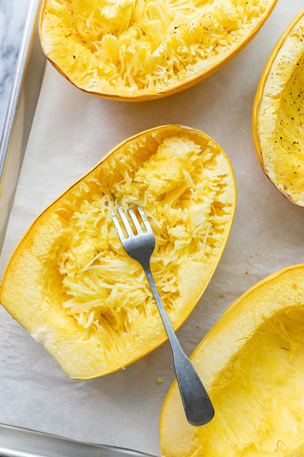 top down view of halved and baked spaghetti squash with fork on metal sheet pan.