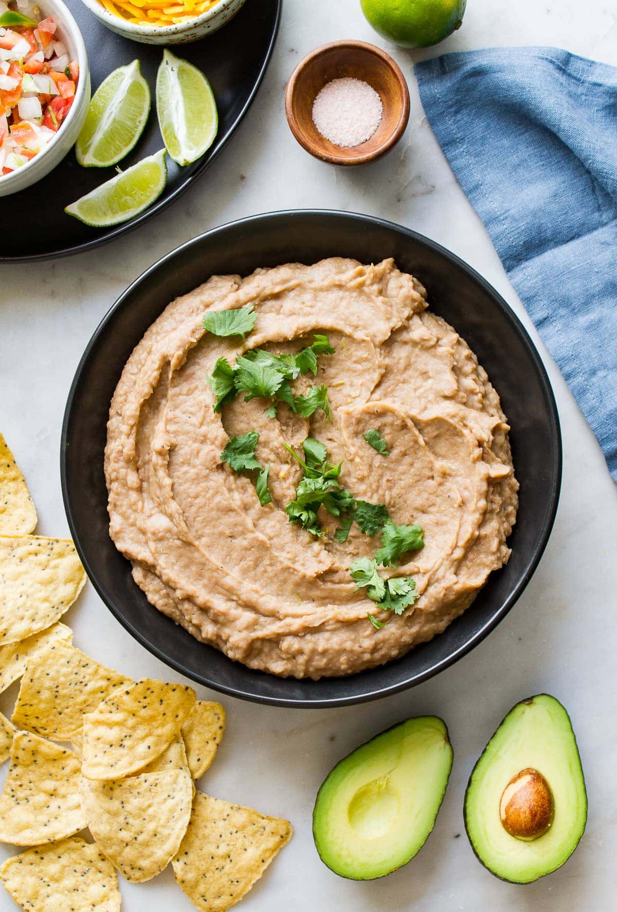 top down view of refried beans in a white serving bowl with chopped cilantro sprinkled overtop.