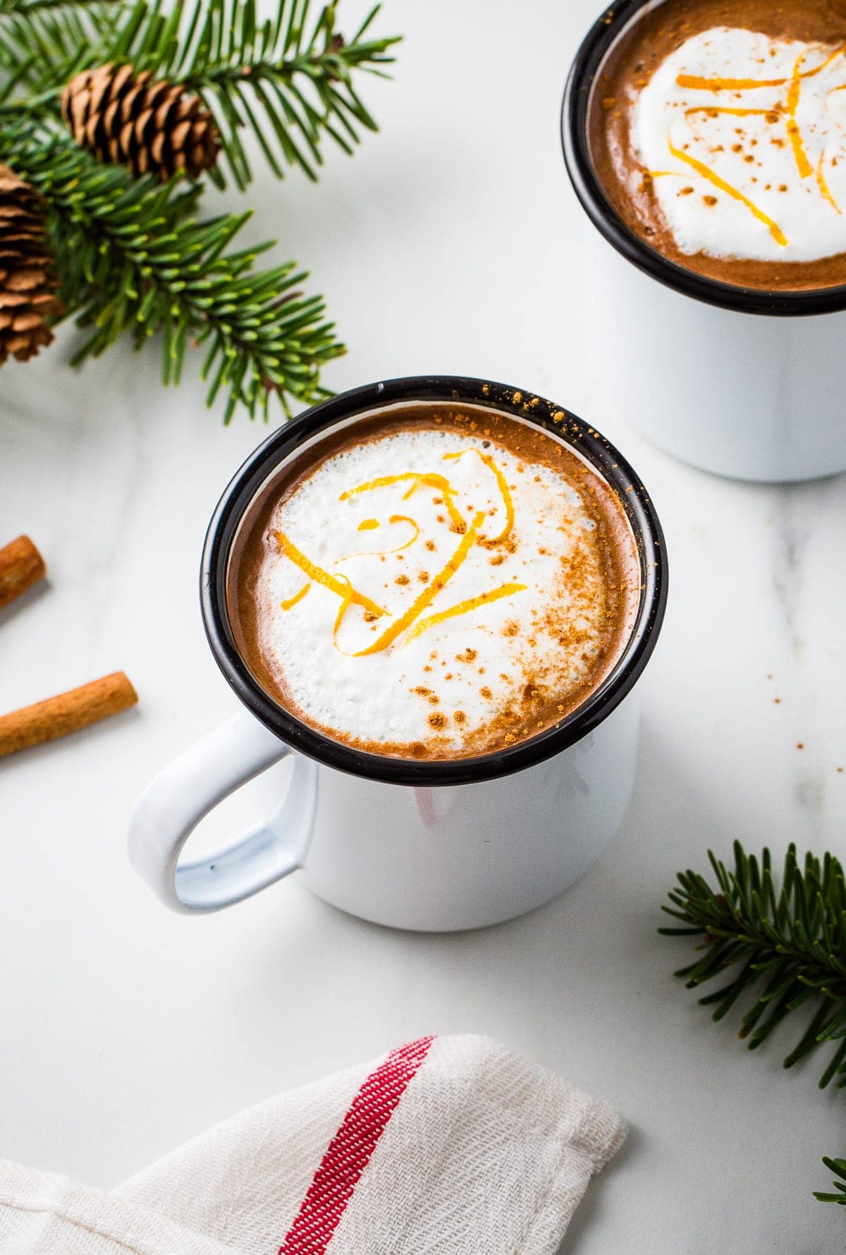 top down view of a orange hot cocoa in a white mug with black rim and surrounded by items.