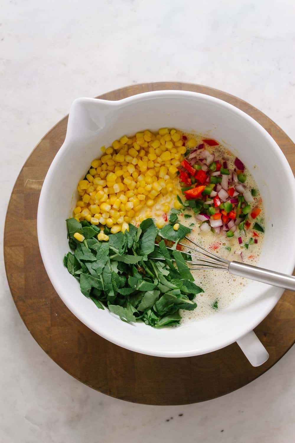 top down view of the process of mixing the chickpea flour frittata batter and adding veggies in a white mixing bowl.