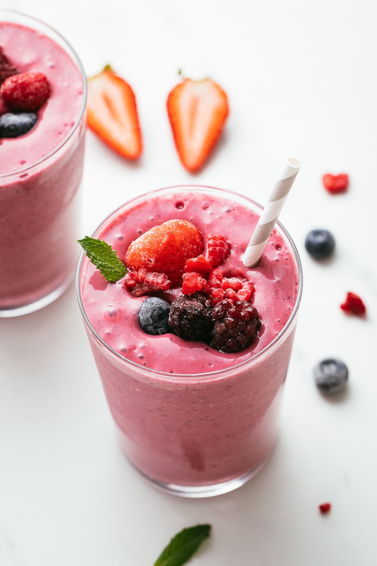 side angle view of healthy mixed berry yogurt smoothie in a glass with straw and items surrounding.