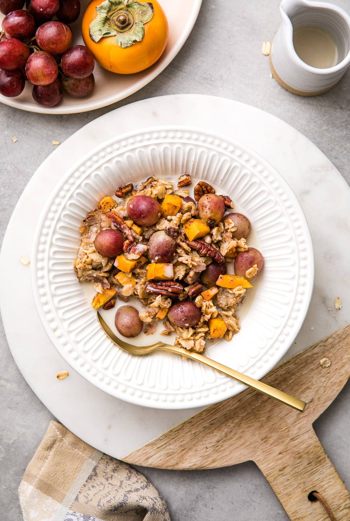 top down view of bowl with serving of baked oatmeal with gold spoon and items surrounding.