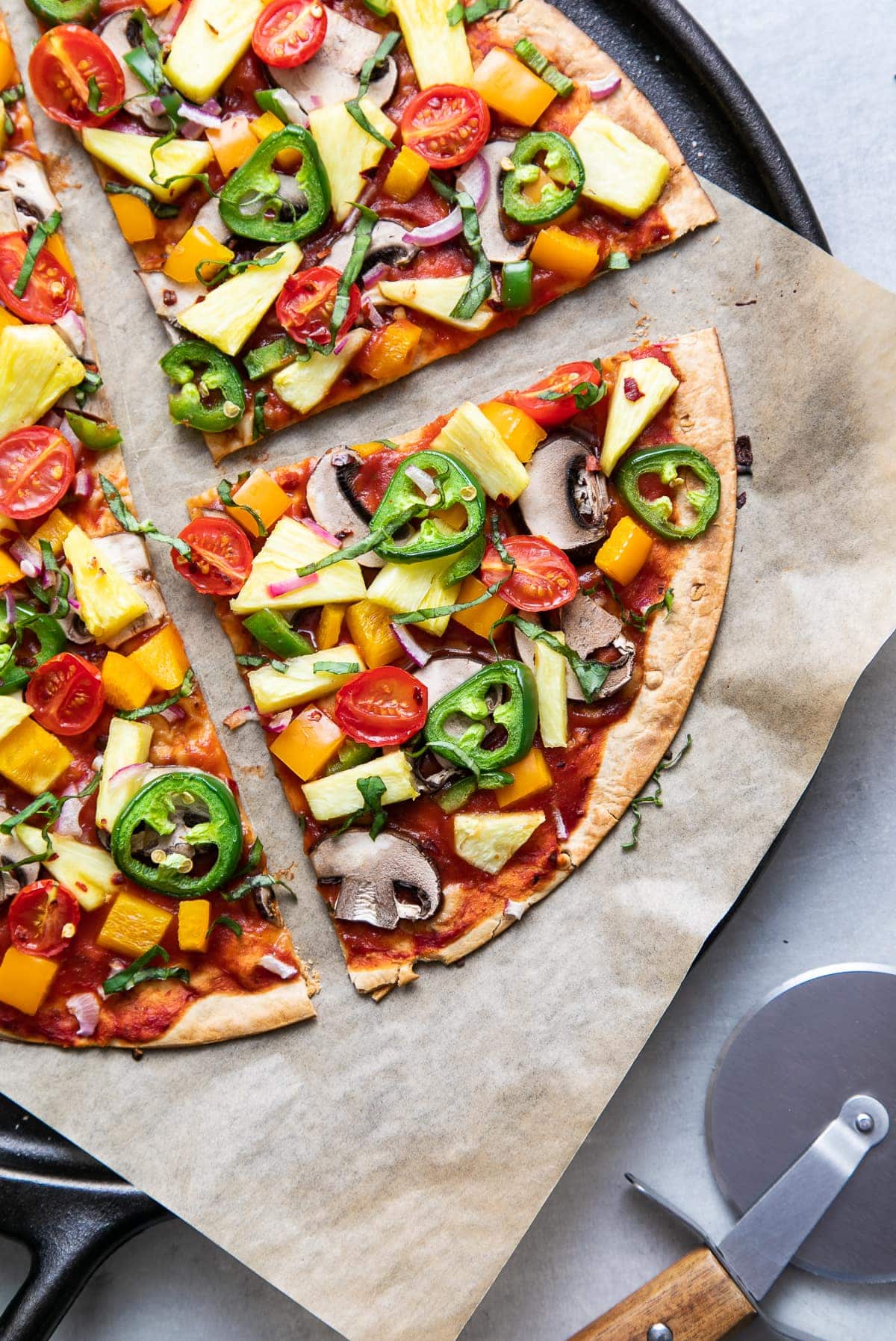 top down view of freshly baked pineapple veggie lovers pizza on a cast iron pizza pan sliced.