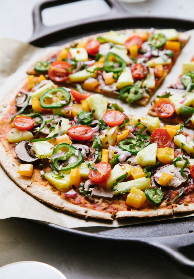 side angle view of freshly baked pineapple veggie lovers pizza on a cast iron pizza pan sliced.