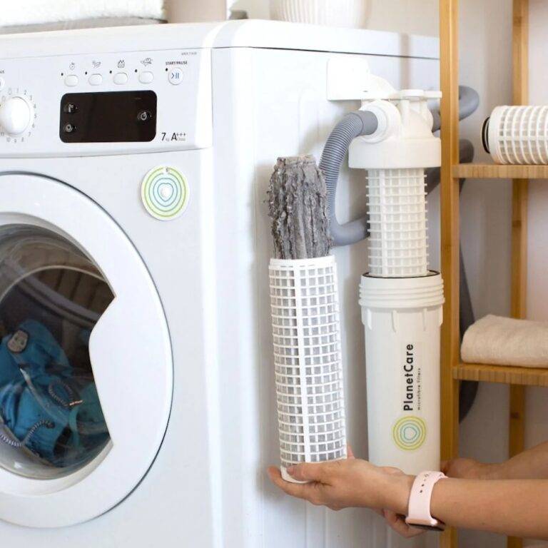 A woman changes out a dirty filter for a clean one in the PlanetCare laundry filtration device installed on her home washing machine.