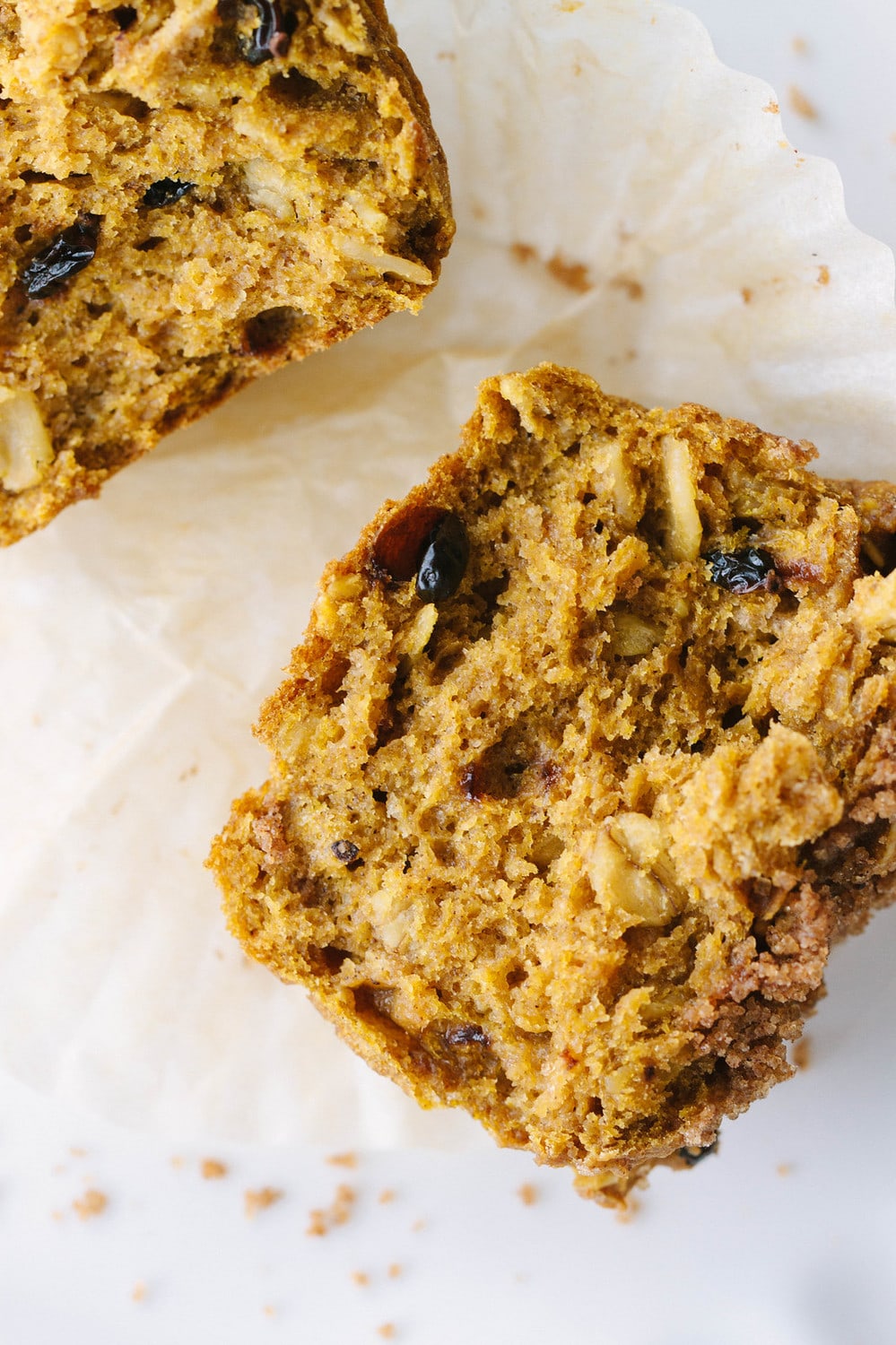 pumpkin oat muffin split in half laying on the its paper liner on a marble slab