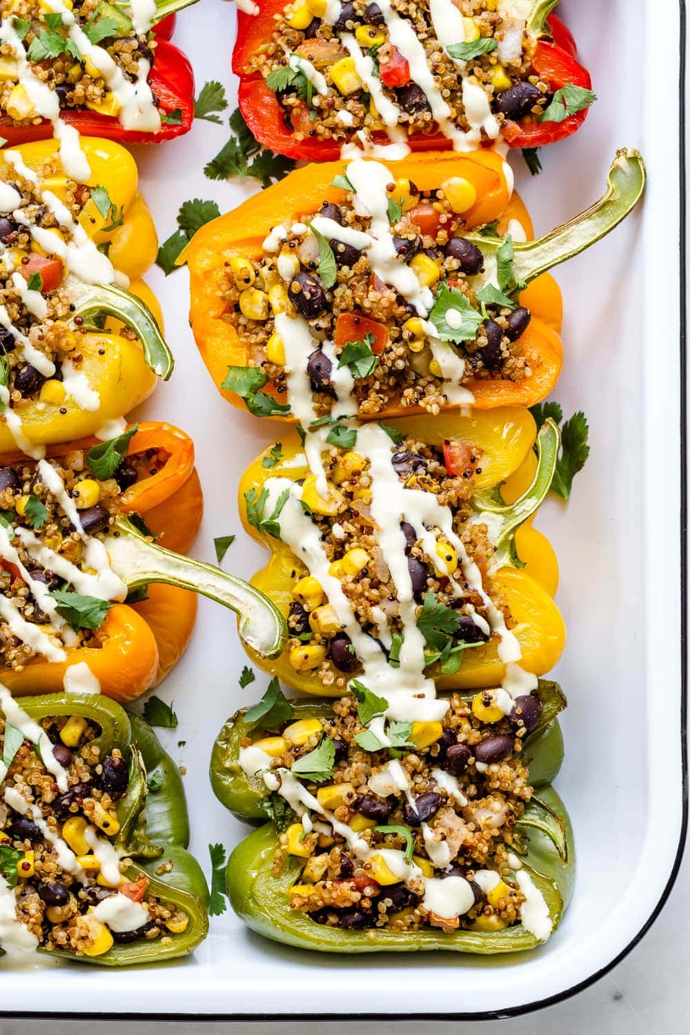 top down view of quinoa stuffed colored bell peppers on a serving dish topped with vegan cashew cheese sauce.