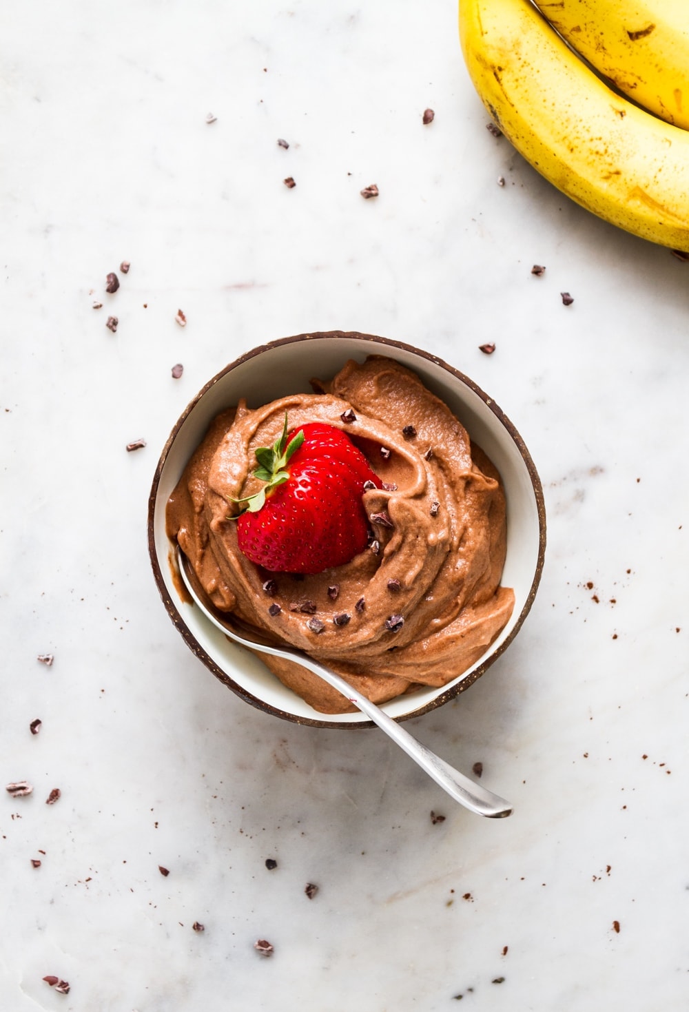 top down view of a bowl with raw vegan chocolate banana ice cream with sliced strawberry and a spoon.