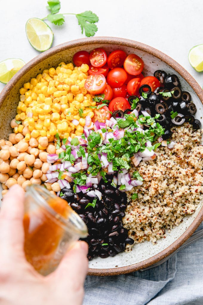 top down view of chili-lime dressing being poured overtop southwest quinoa salad.