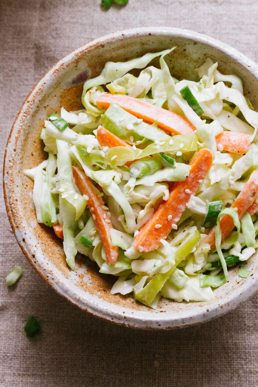 top down view of a small handmade bowl with a serving of spicy vegan coleslaw with creamy tahini dijon dressing, topped with sesame seeds.