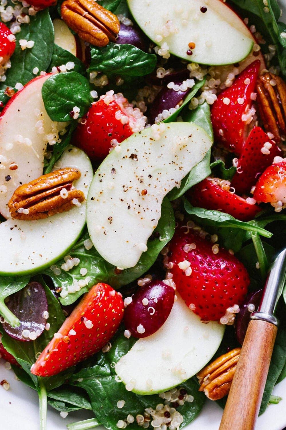 up close view of spinach salad with strawberries, apple and quinoa.