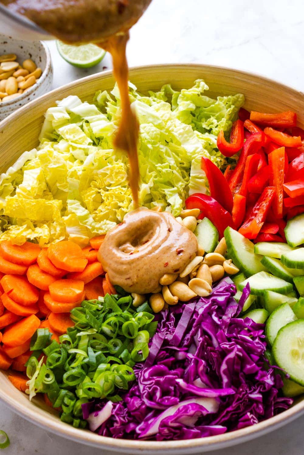 side angle view of thai peanut dressing being poured over top of the salad ingredients in a large bowl