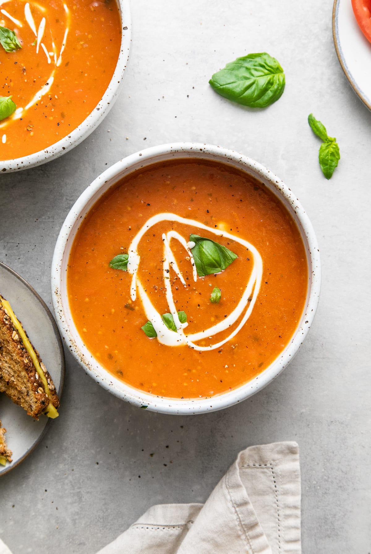 top down view of bowl with serving of tomato basil soup and items surrounding.